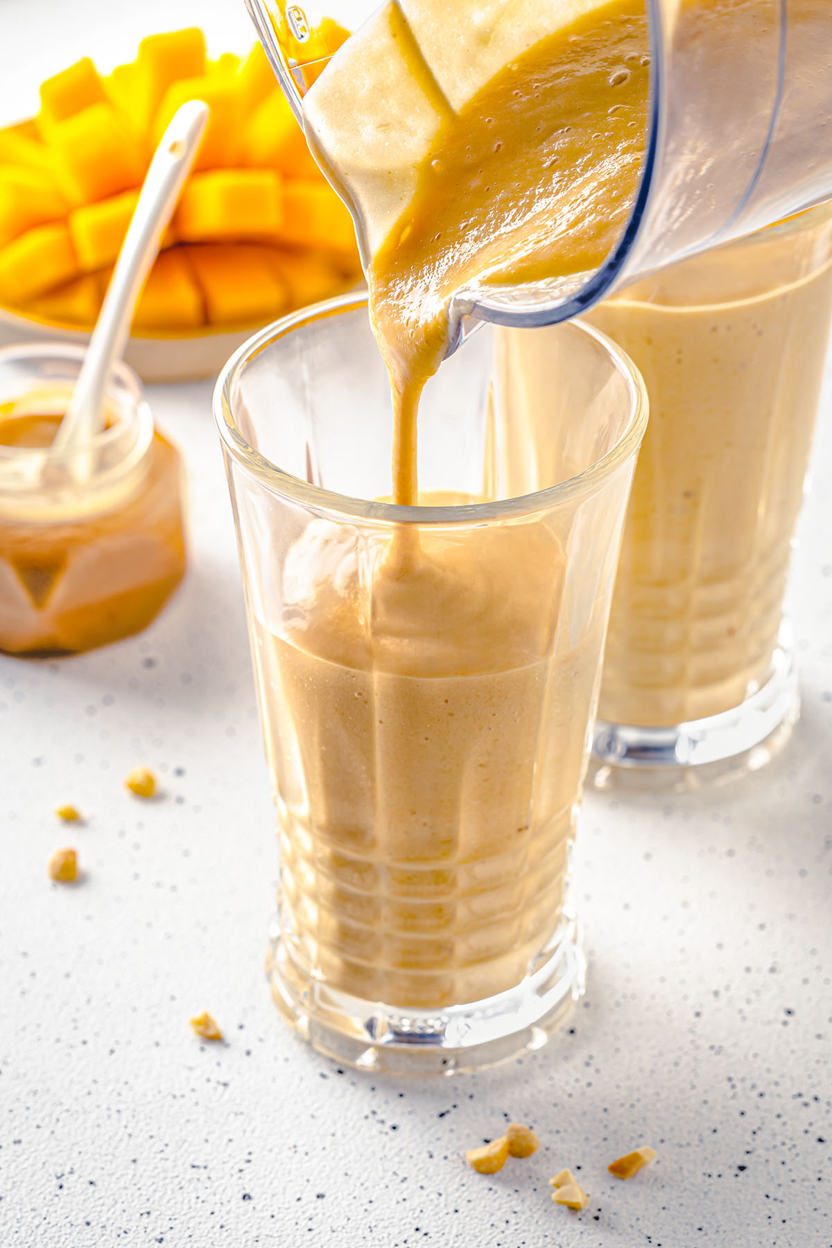 Pouring mango peanut butter smoothie in a glass
