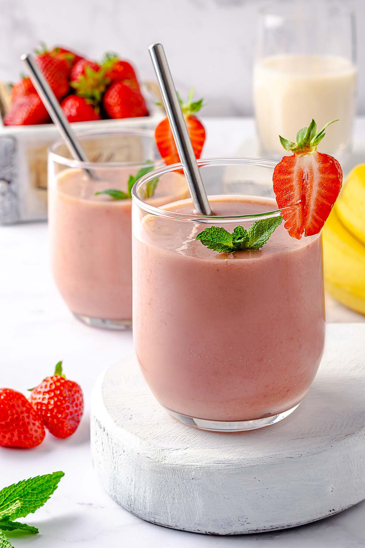 A glass with strawberry banana avocado smoothie on a white wooden board