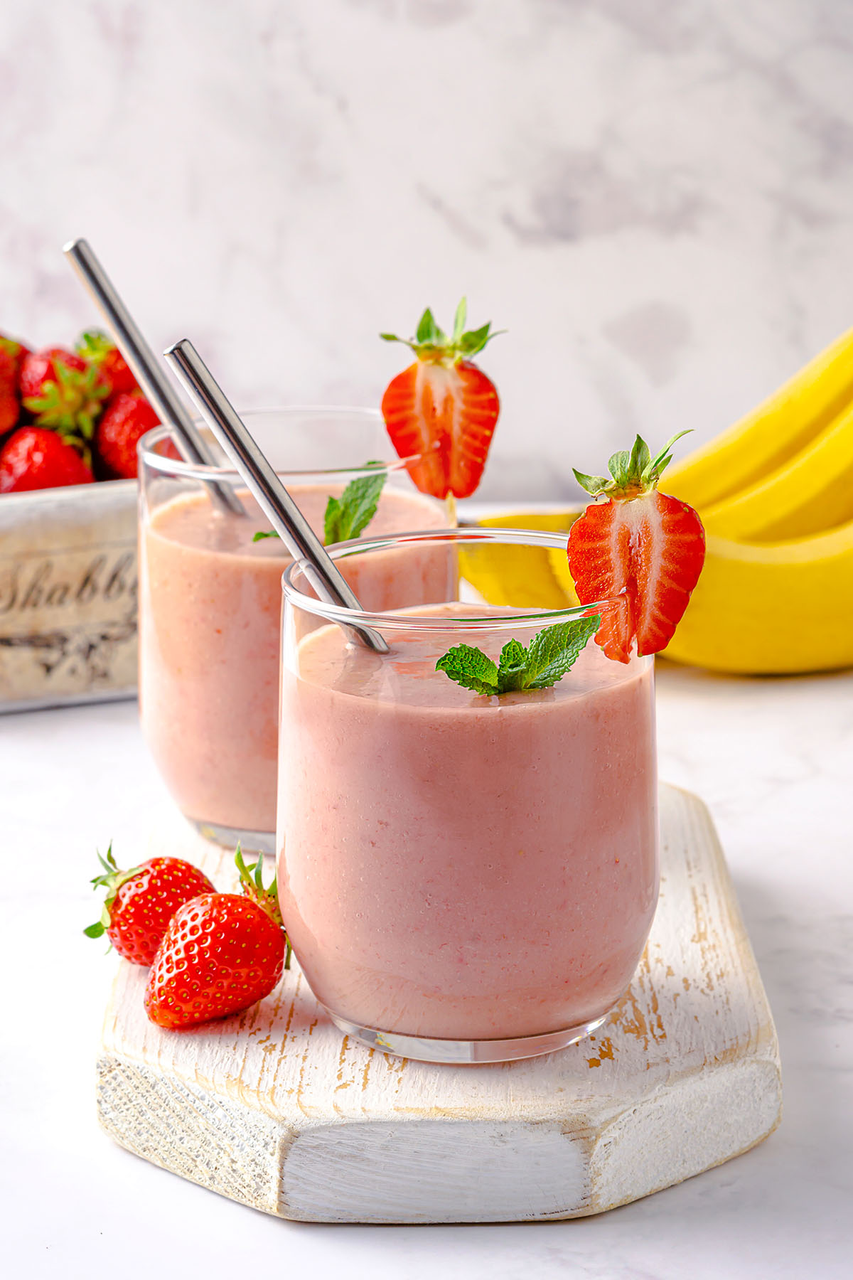 Two glasses of strawberry banana avocado smoothie decorated with mint and strawberry