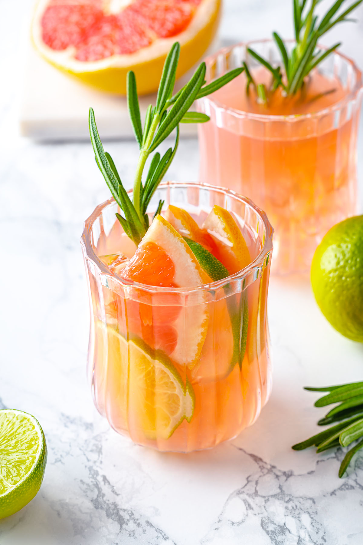 Two glasses with pink grapefruit mocktail decorated with lime and rosemary