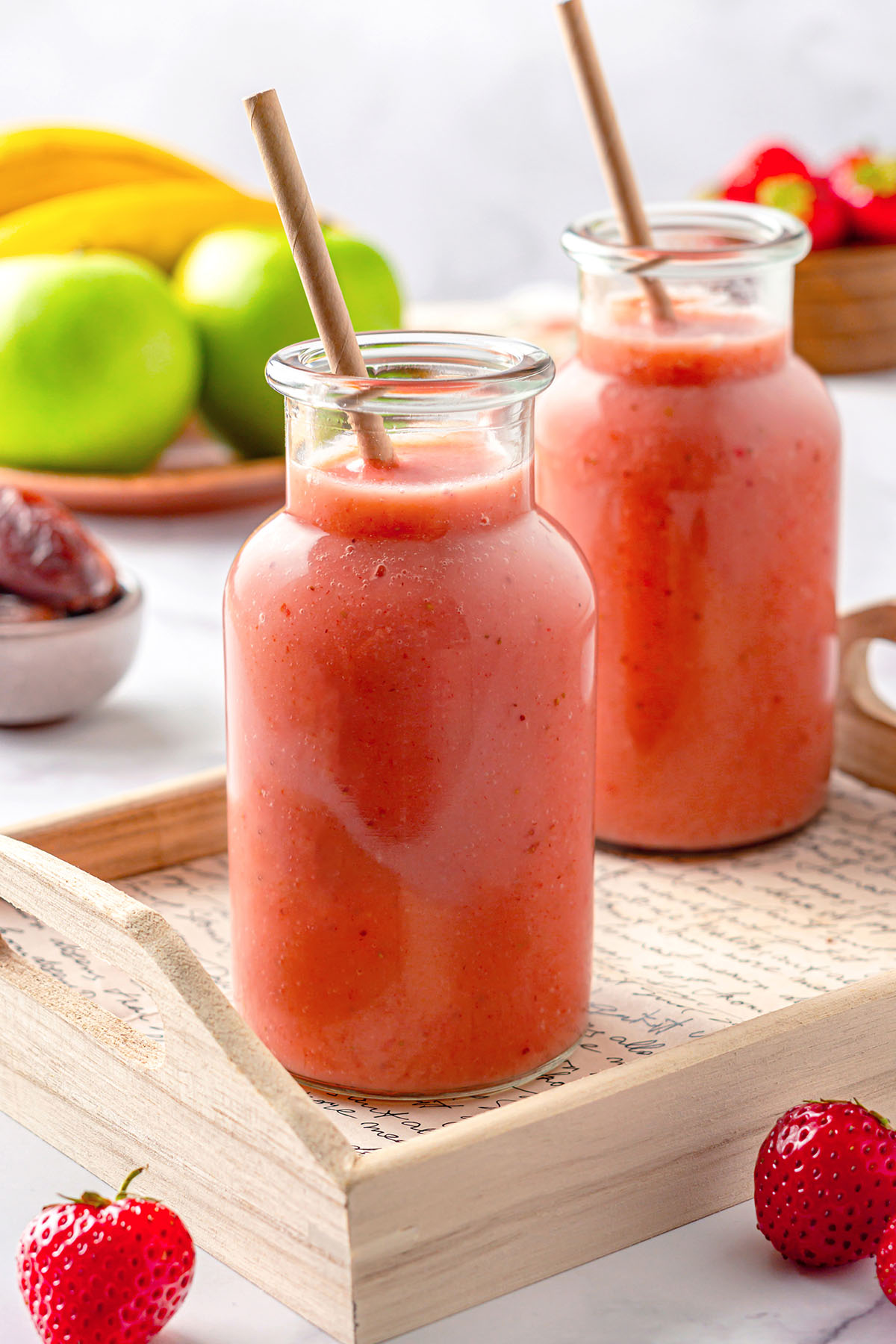 Two strawberry apple smoothie bottles on a wooden tray