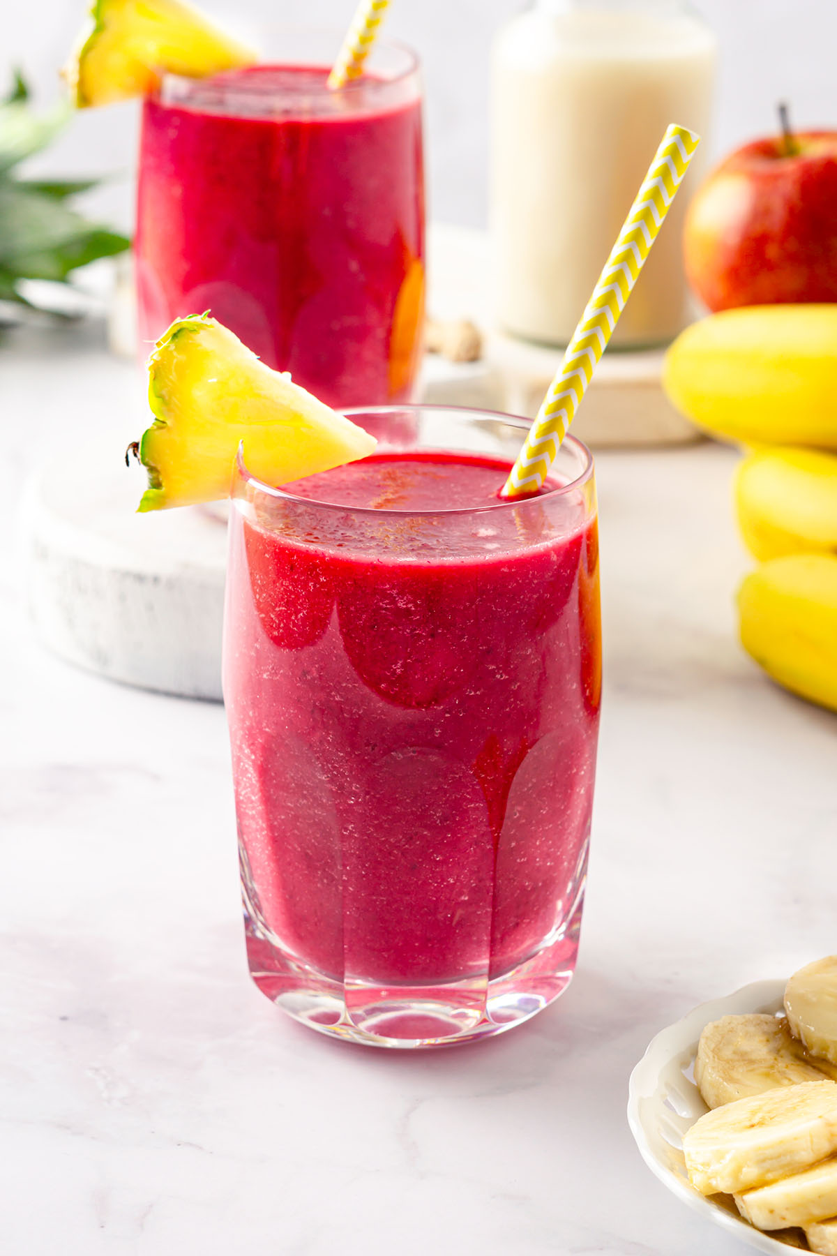 Glass with beet pineapple smoothie decorated with pineapple slice