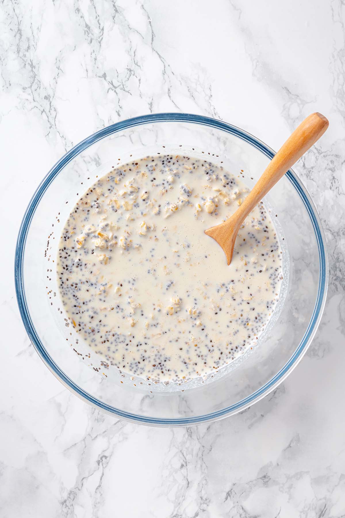 Process of making overnight oats showing all ingredients in a bowl with wooden spoon