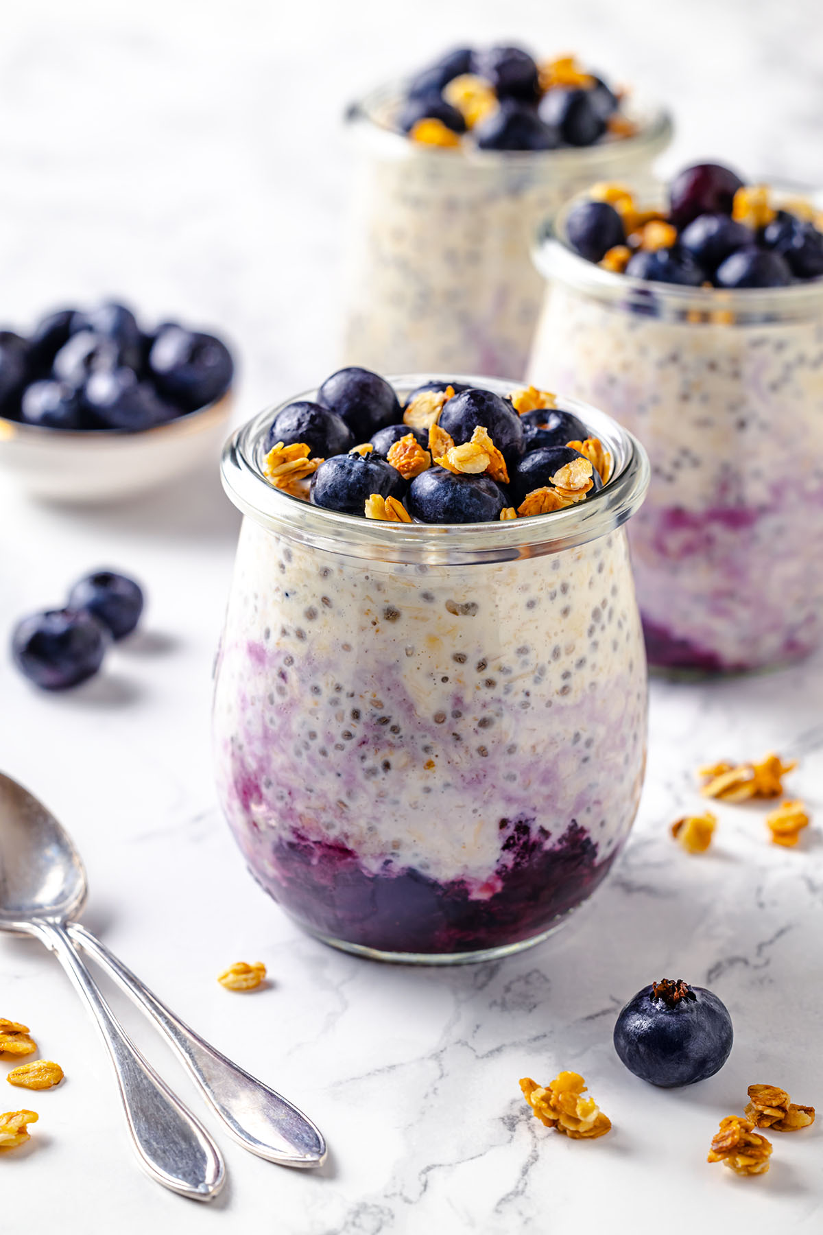 Three jars with blueberry cheesecake overnight oats decorated with frozen blueberries