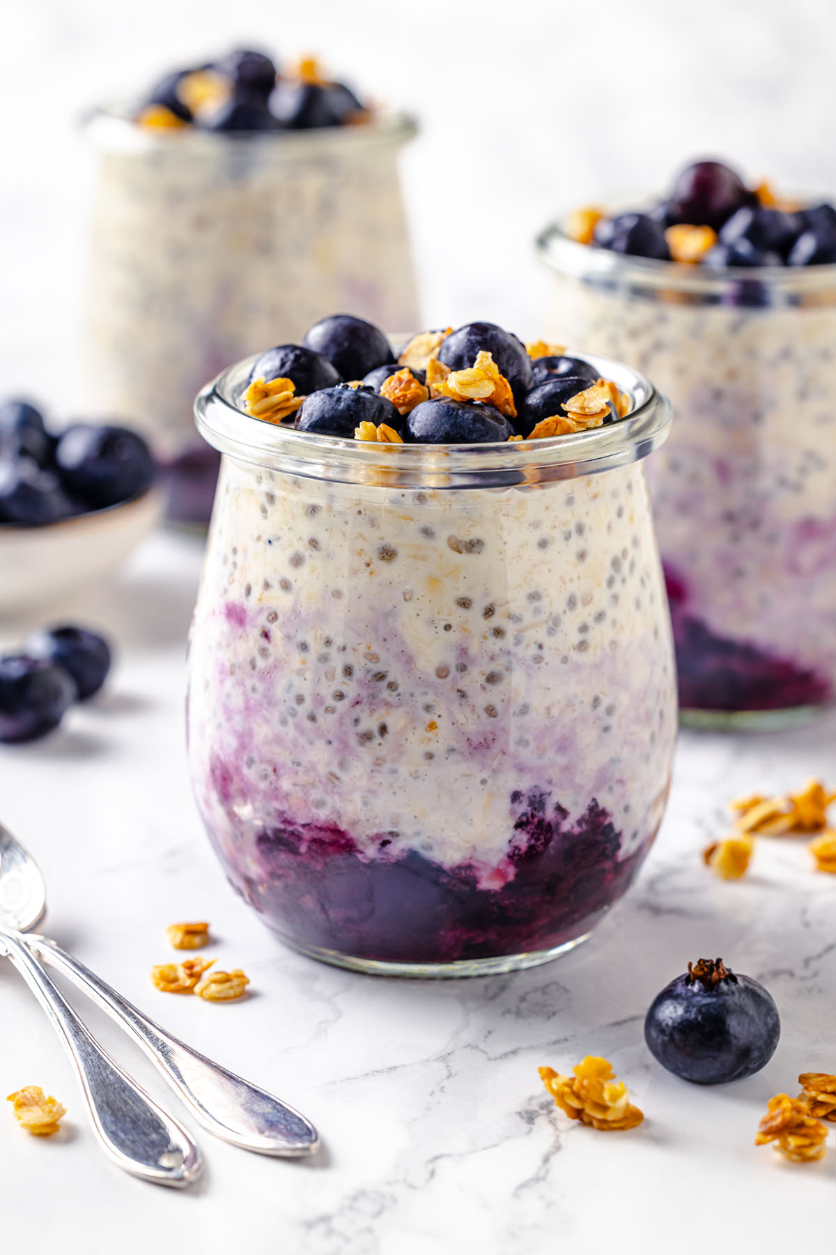 Three jars with blueberry cheesecake overnight oats decorated with granola and blueberries