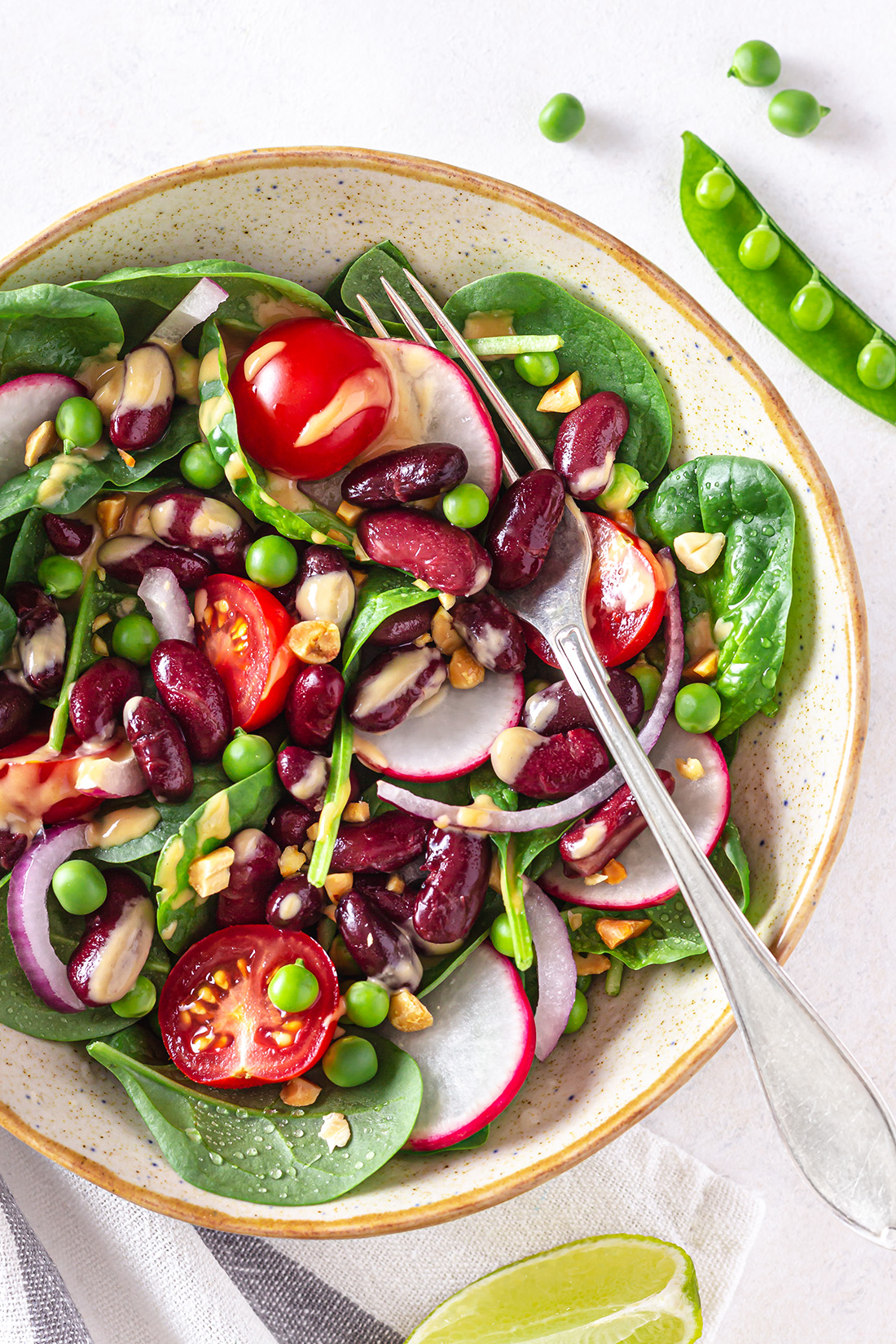 Salad with kidney beans, veggies and peanut dressing  in a serving plate with a fork