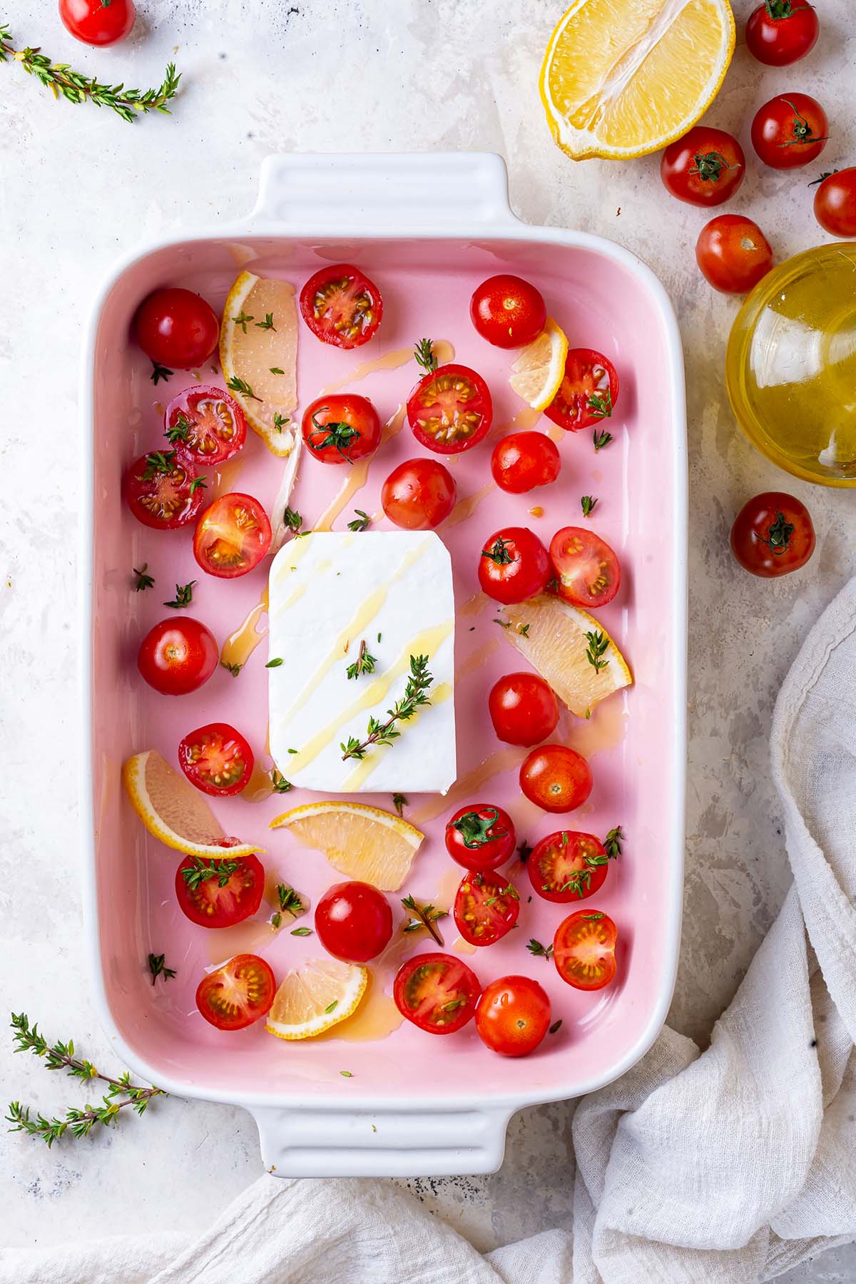 Block of feta, cherry tomatoes thyme and lemon slices in a baking dish