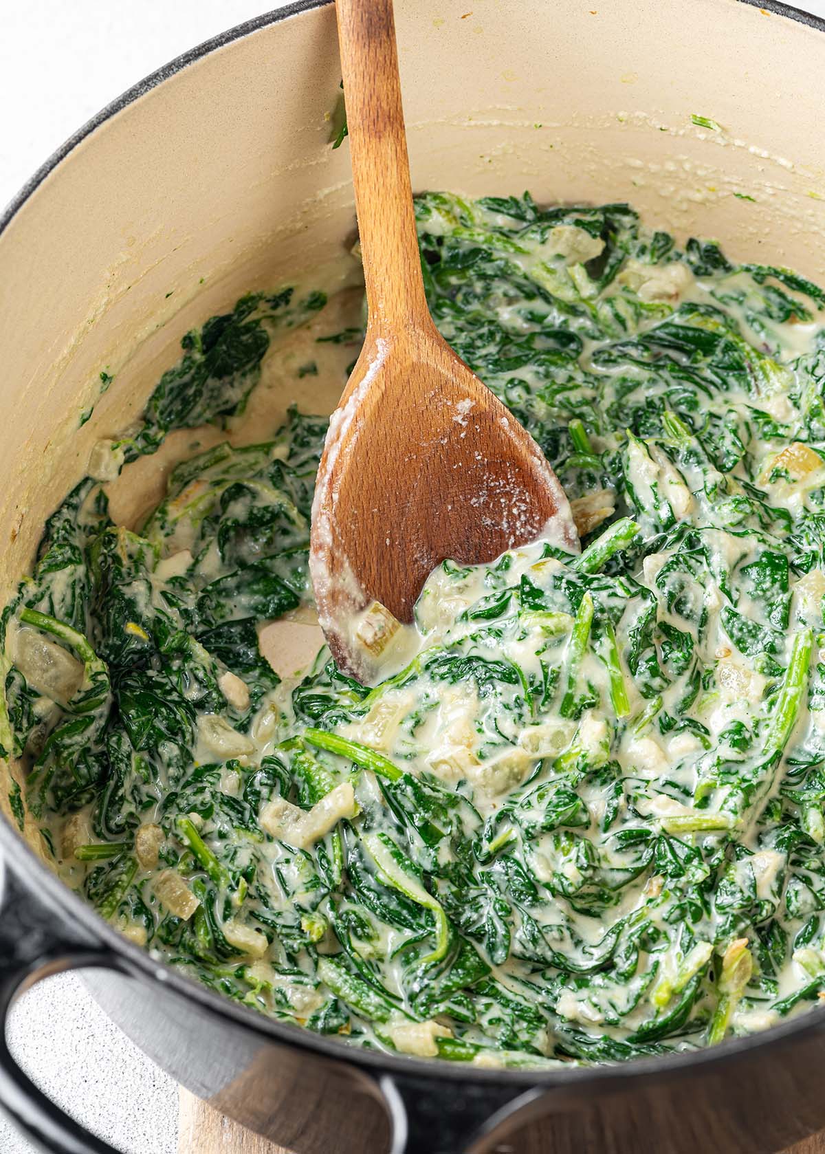 Vegan creamed spinach with cashews in a pot with a wooden spoon