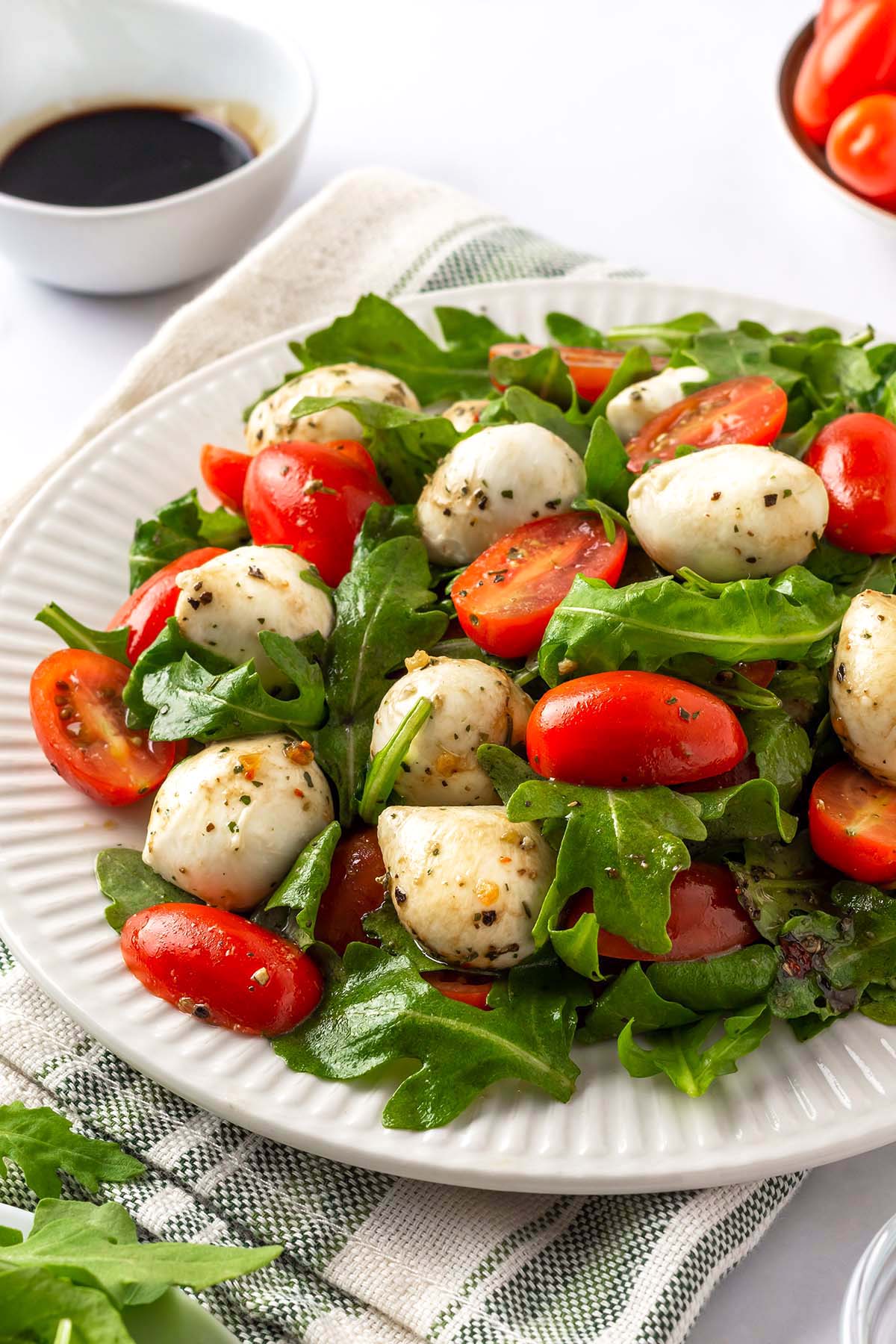 Arugula caprese salad with mozzarella balls and cherry tomatoes on a white serving plate