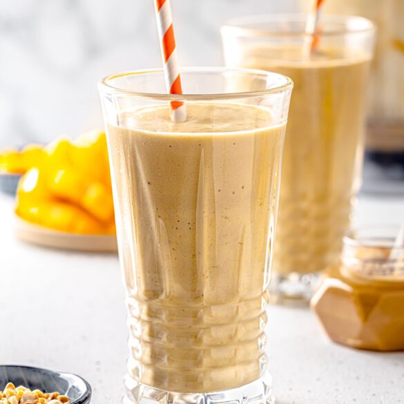 Mango peanut butter smoothie in a glass with paper straw