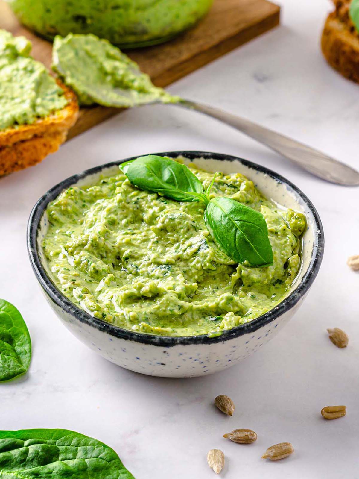 Green sunflower seed pesto in small bowl, decorated with fresh basil