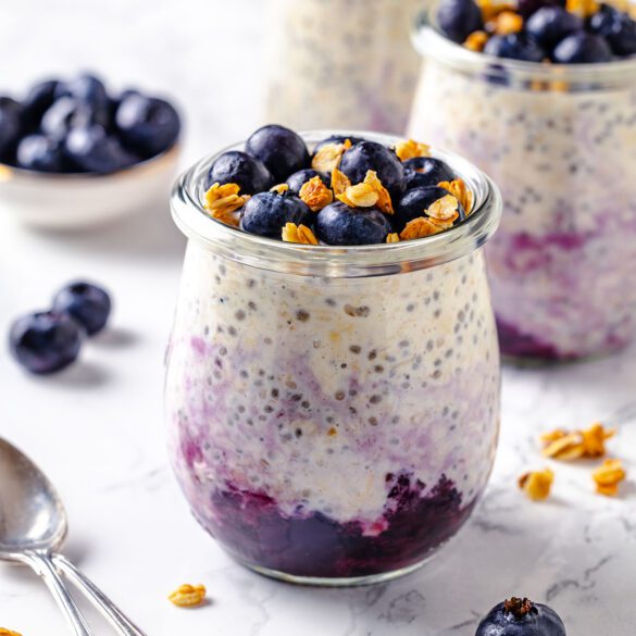 Three jars with blueberry cheesecake overnight oats decorated with frozen blueberries